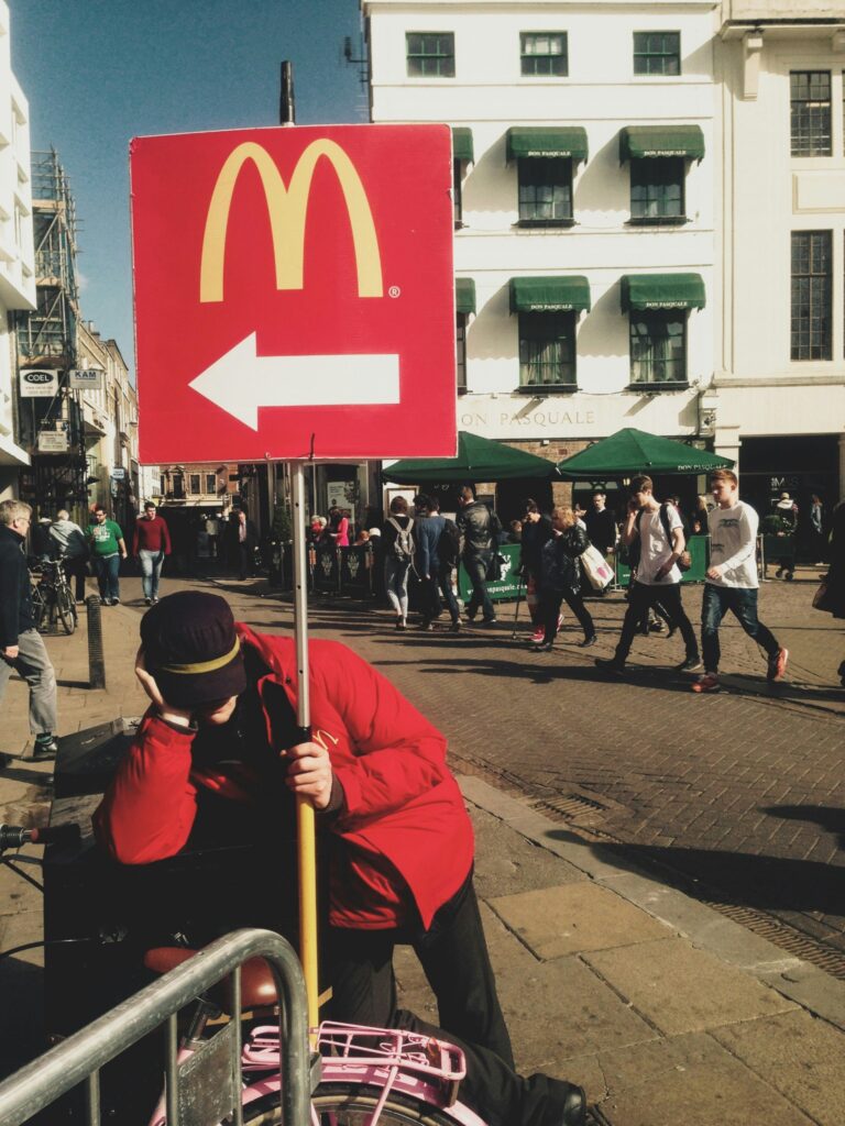 Worker holding a McDonald's direction sign on a busy street