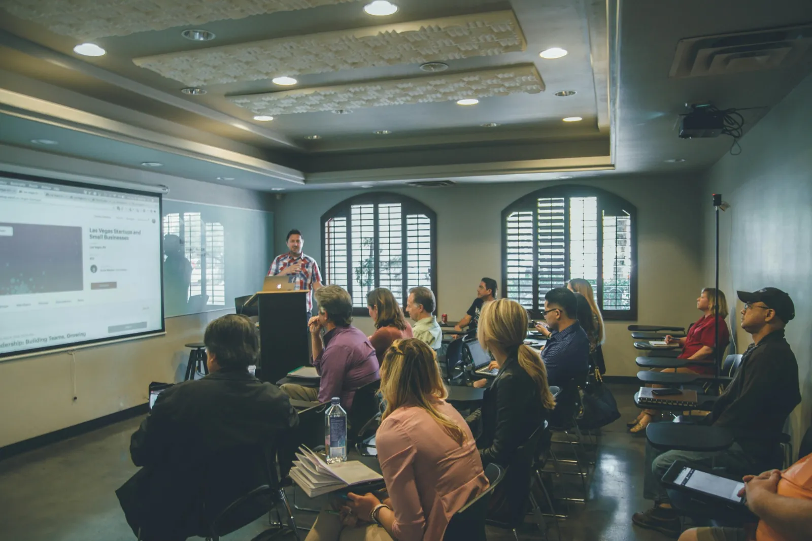 Audience seated at tables watching a presentation in a training room