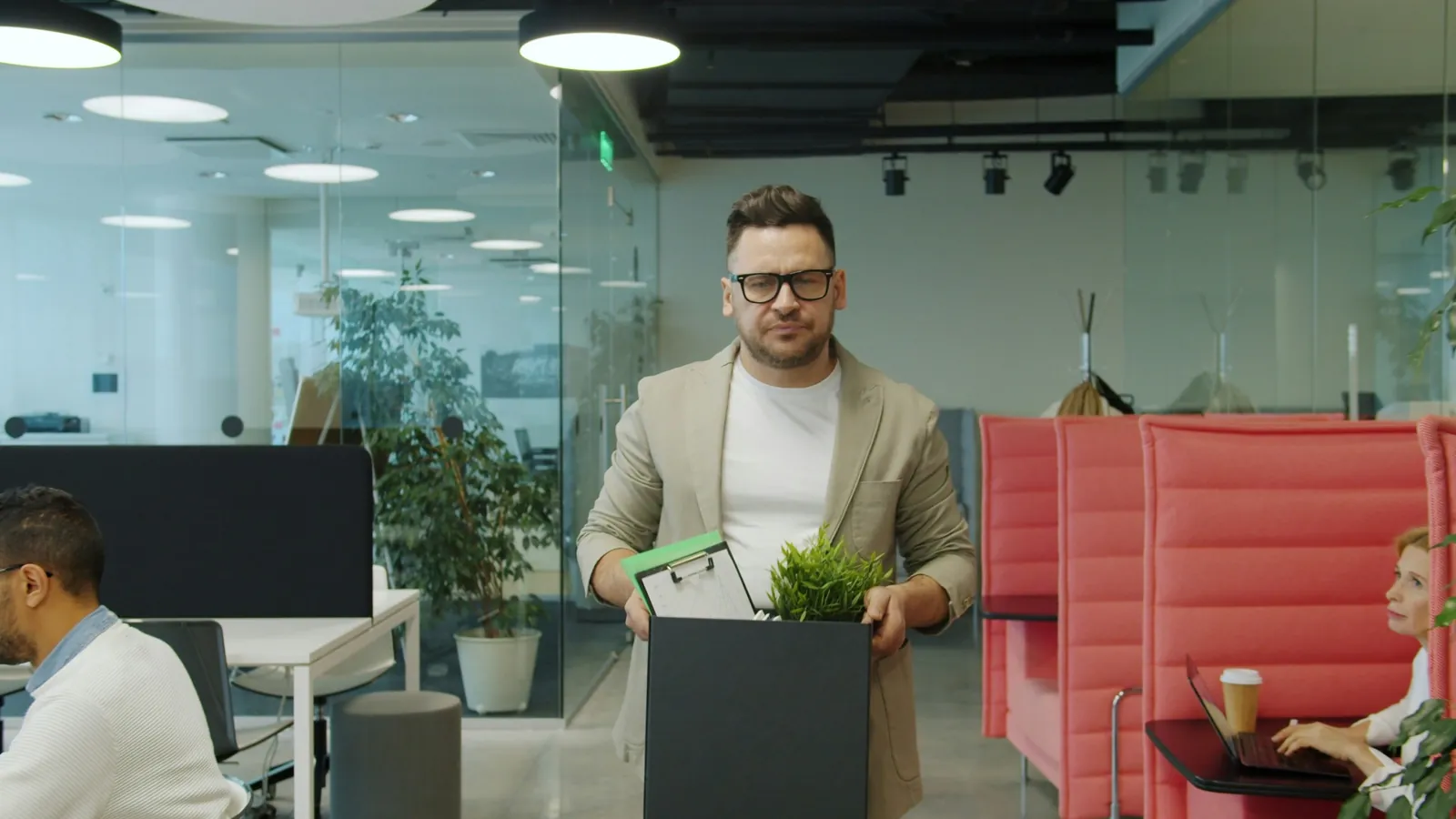 Man carrying a cardboard box containing a plant and other belongings in an office