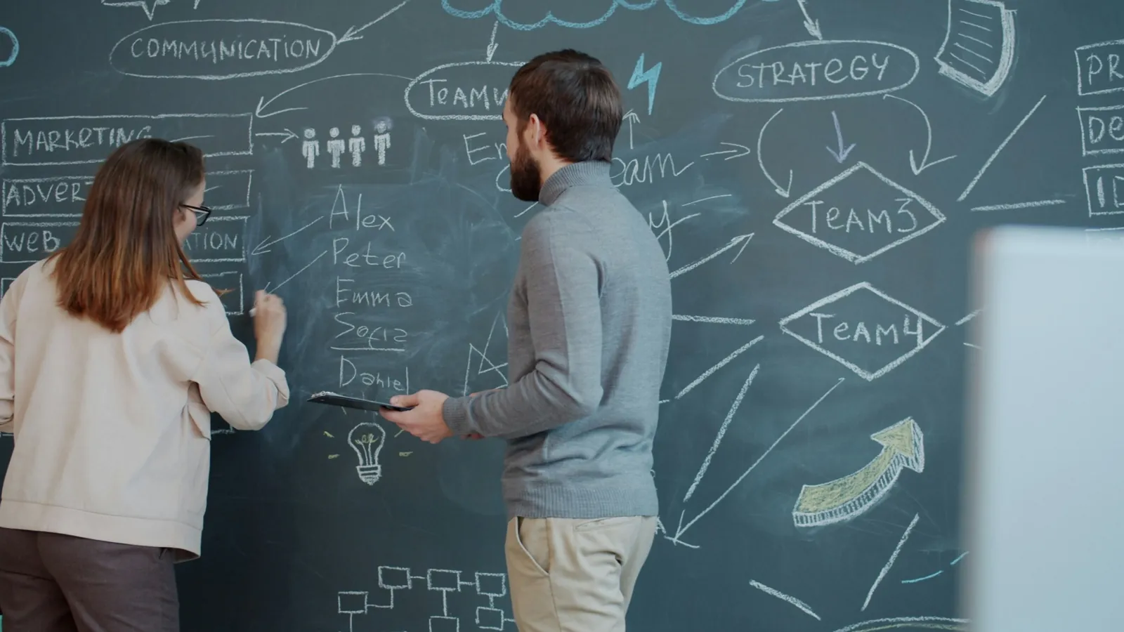 Two people discussing diagrams and notes on a chalkboard
