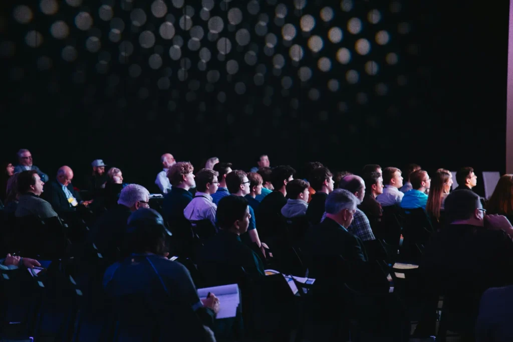 Seated audience facing a presentation in a darkened room