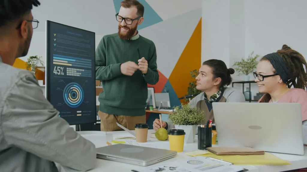Colleagues discussing charts on a monitor around an office table