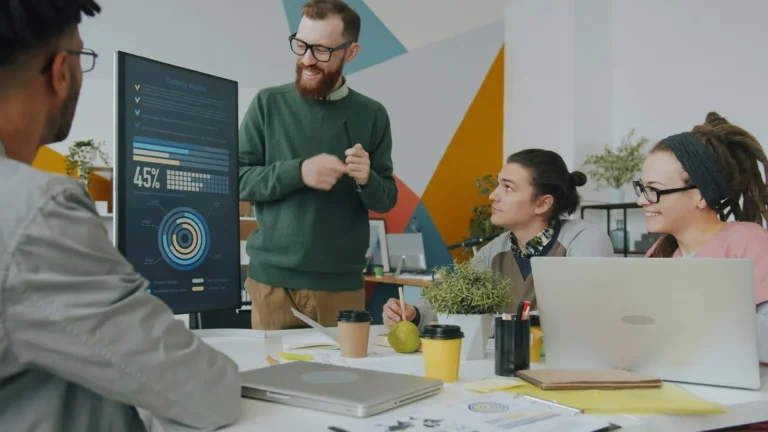 Colleagues discussing charts on a monitor around an office table