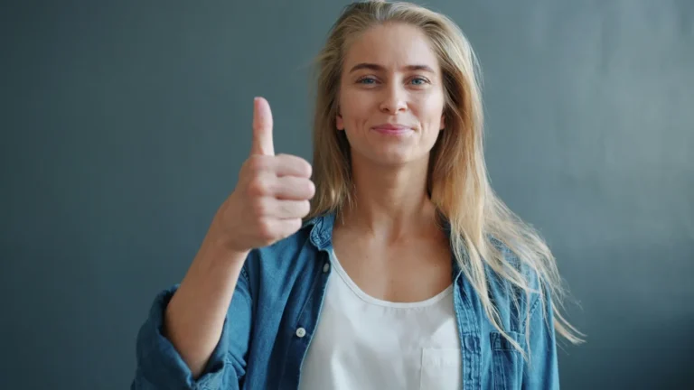 Woman in a denim shirt giving a thumbs-up against a gray background