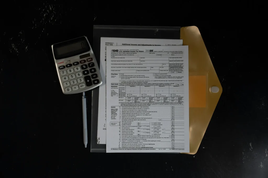Printed financial forms beside a calculator on a dark desk.