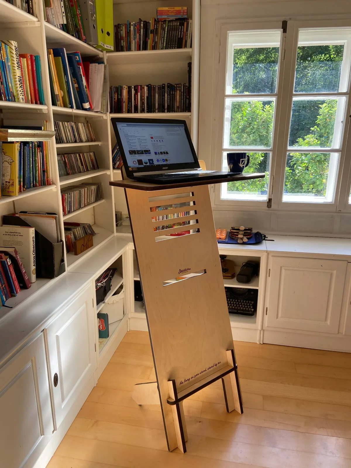 A laptop on a wooden standing desk in a home workspace.