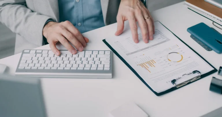 A person reviewing printed charts beside a keyboard and clipboard.
