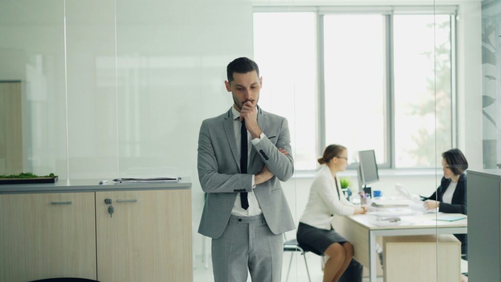 Office worker standing thoughtfully while colleagues work nearby