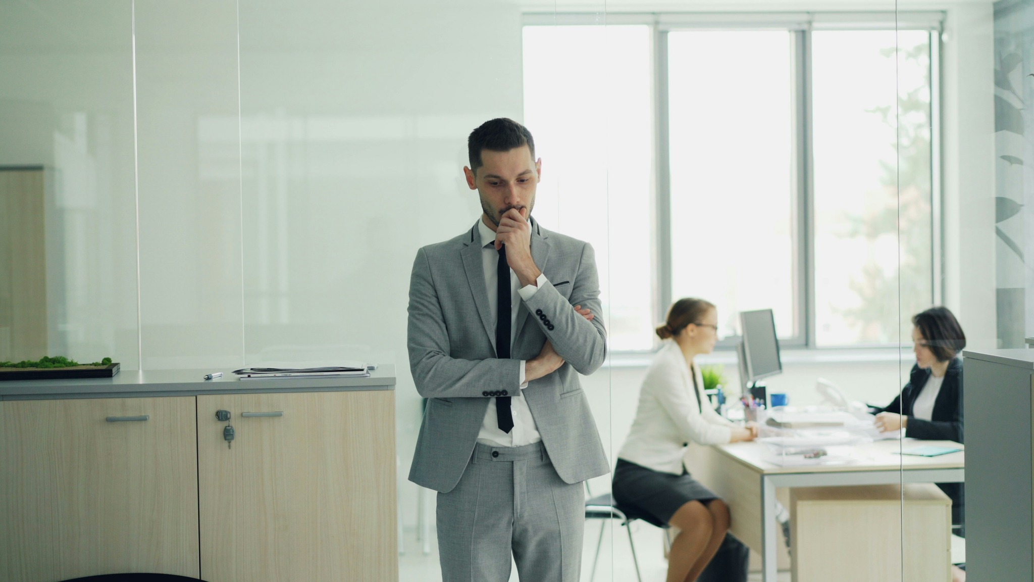 Office worker standing thoughtfully while colleagues work nearby