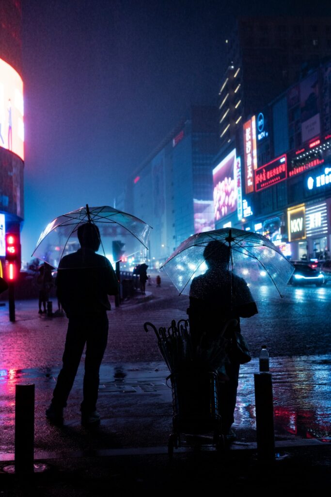 People with umbrellas on a neon-lit city street at night